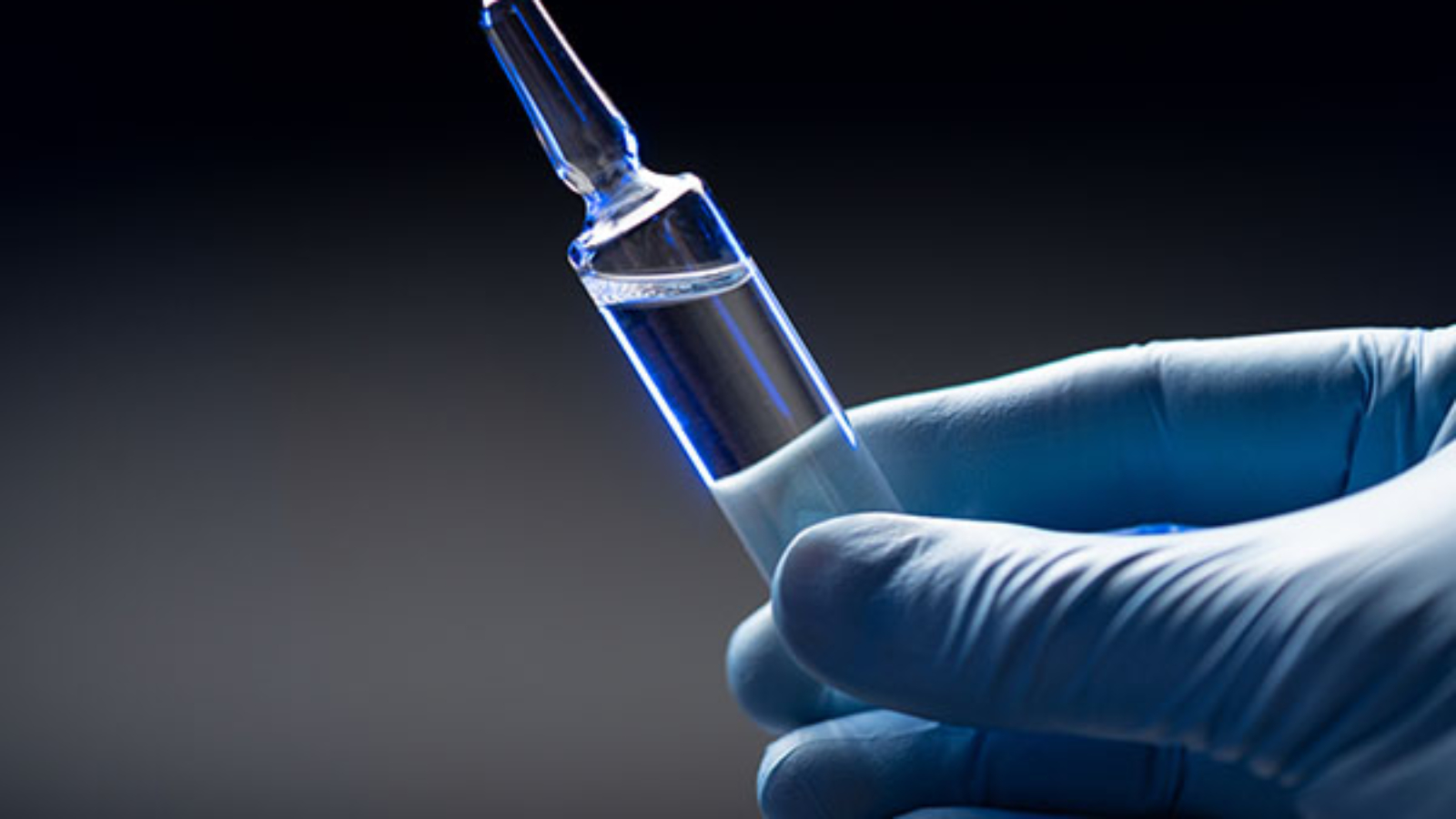 Hand in blue medical gloves holds an ampoule with a coronavirus vaccine. Coronavirus vaccination concept