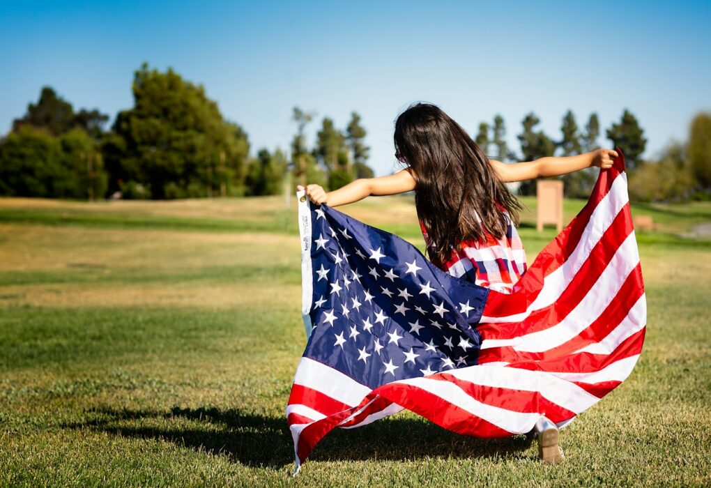 girl holding US flag on grassland